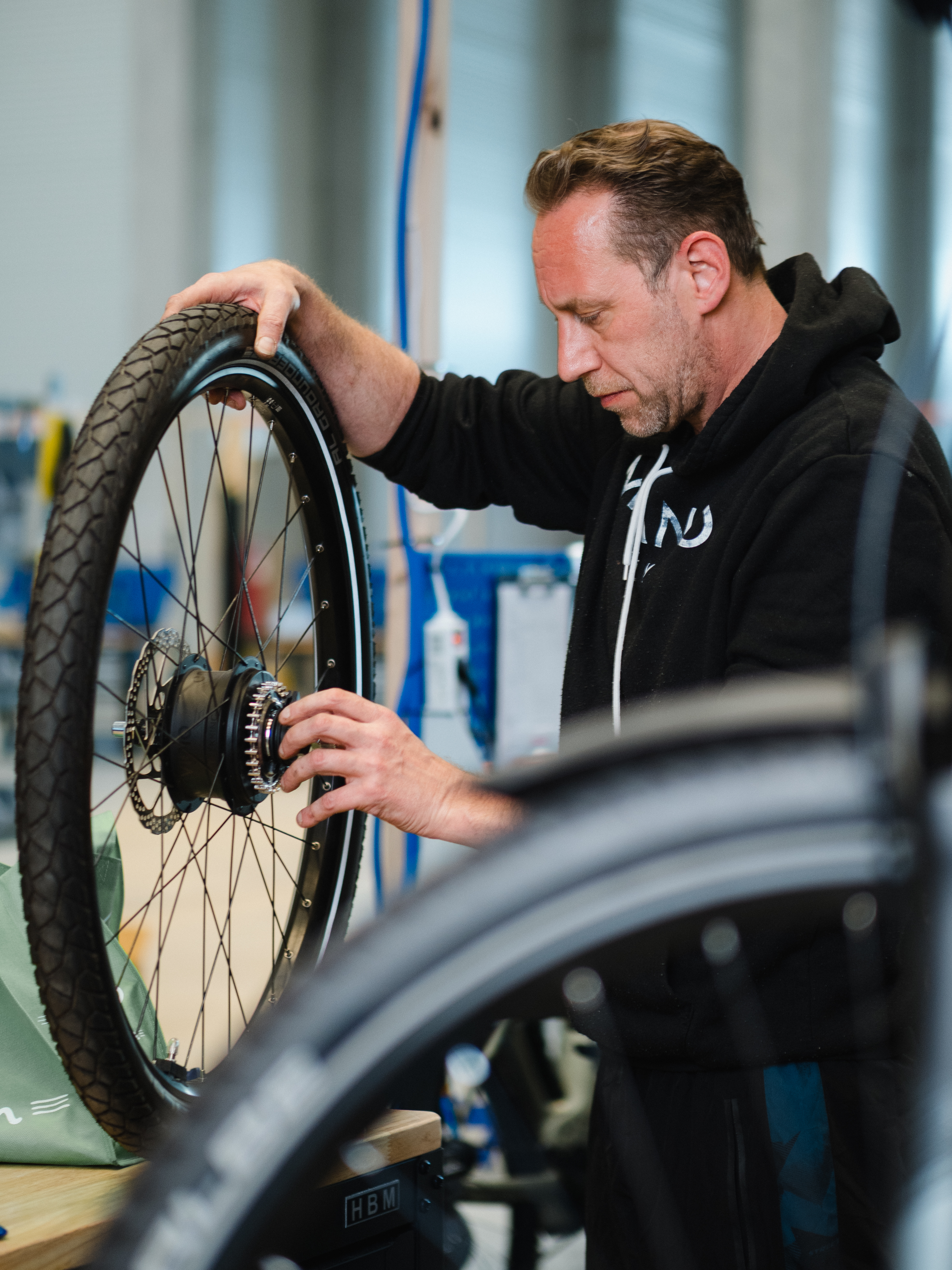 Authentische Arbeitswelt-Fotografie: Ein Zweiradmechaniker arbeitet mit höchster Präzision an einem E-Bike-Laufrad. Das Bild vermittelt handwerkliche Qualität und die Leidenschaft für moderne Mobilitätslösungen in einem professionellen Werkstatt-Umfeld.