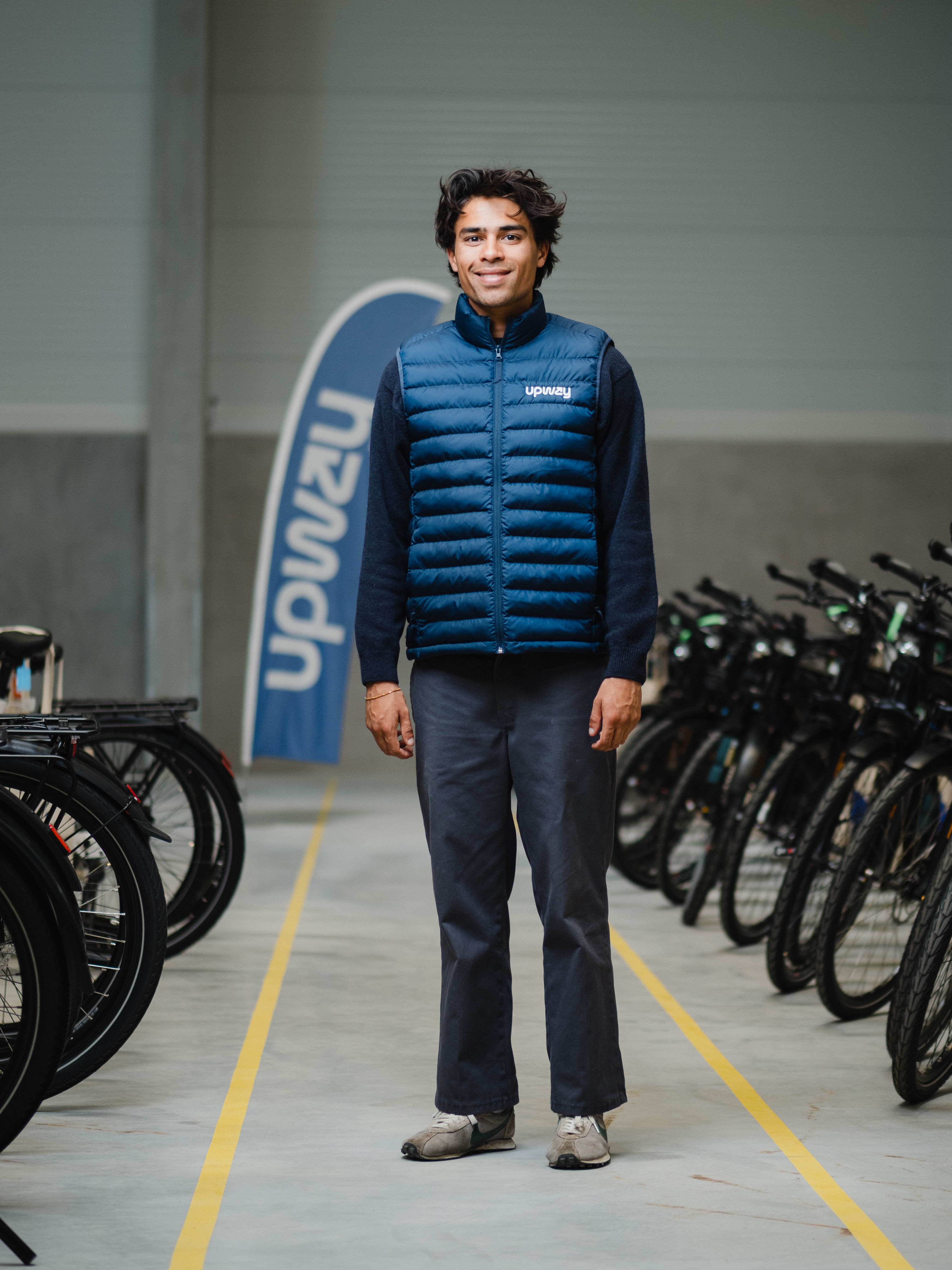 Modernes Mitarbeiterportrait im Corporate Design: Ein sympathischer Mitarbeiter in Upway-Arbeitskleidung präsentiert sich selbstbewusst in der Logistikhalle. Das Bild verkörpert Professionalität, Teamzugehörigkeit und die moderne Arbeitswelt eines E-Mobility-Unternehmens.